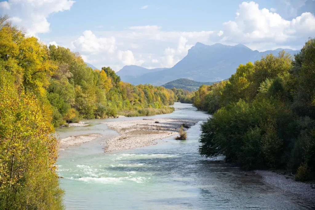 La rivière Drôme bordée d’arbres, avec les montagnes en arrière-plan